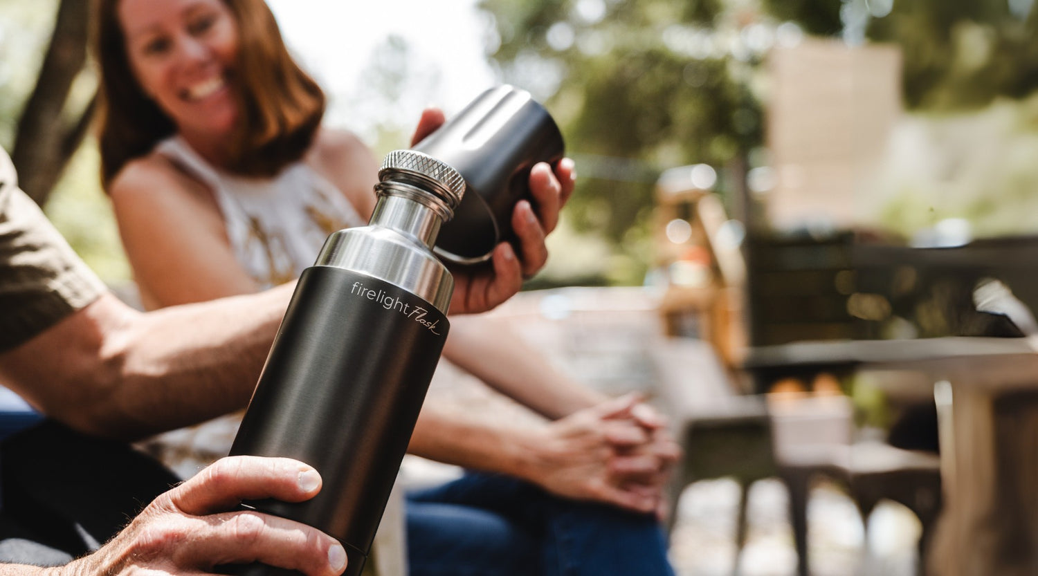 Person holding a black Firelight Flask with a blurred outdoor background.